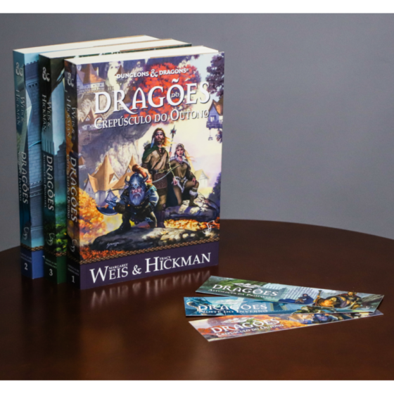 Três livros e 3 marcadores de páginas das Crônicas de Dragonlance sobre mesa de madeira